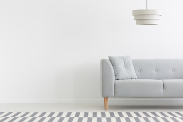 Lamp above grey couch in white minimal apartment interior with copy space on empty wall. Real photo - obrazy, fototapety, plakaty