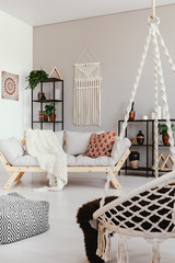 Warm ethno living room with comfortable couch, metal shelves and macrame on the wall, real photo