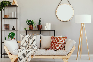White wooden lamp next to stylish scandinavian couch with patterned pillow and blanket in elegant...