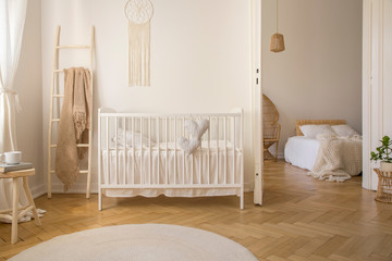Wooden ladder with beige blanket on it, next to white crib with pillows, real photo