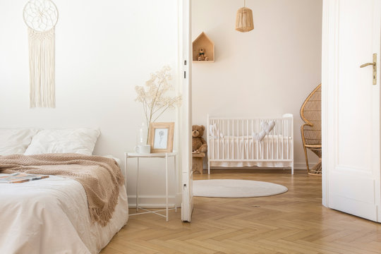 White scandinavian bedroom with door open to nursery with crib and toys, real photo