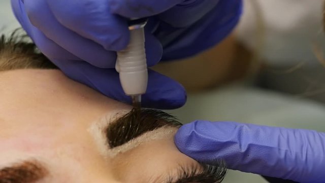 close-up hands of the master doing brows tattoo. permanent eyebrow makeup. slow motion