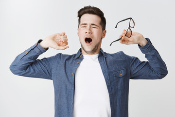Portrait of tired attractive male student taking off glasses closing eyes and yawning while...