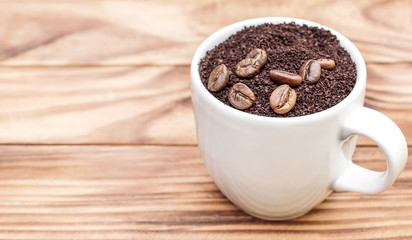 Full cup of ground coffee with coffee beans on the table.