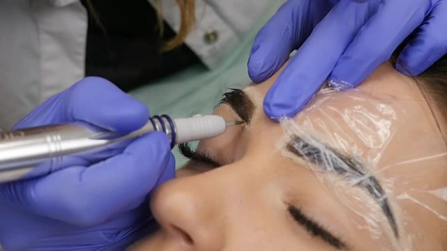 Young beautiful woman getting eyebrows tattoo. permanent makeup for eyebrows at beauty salon. slow motion