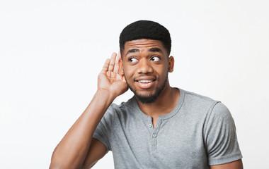Curious african-american man holding hand near ear