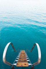 Ladder leading into the refreshing crystal water of a sea. Wooden steps to turquoise ocean water