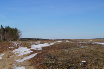 Country field road, slightly powdered with snow and bright blue sky in late autumn on a Sunny day