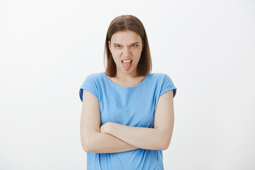 Obraz premium Portrait of nasty disobedient childish woman in blue t-shirt, looking from under forehead and frowning, holding hands crossed on chest, being displeased and disgusted, expressing antipathy
