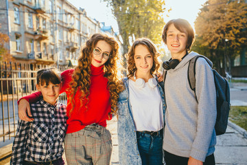 Group portrait of four smiling cheerful teeneger girl and students walking together outdoors in park