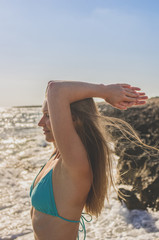 Young happy woman on the sea at sunset raises her arms up