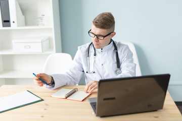 Medicine, working and people concept - handsome doctor sitting at the table and writing a recipe