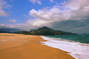 Empty vast sandy beach in Quy Nhohn, Vietnam. Mountains in the background, yellow sand and partly cloudy sky.