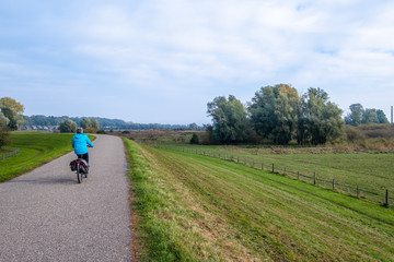Woman on a bicycle on the dike along the flood plains along the river Nederrijn in Wageningen, the Netherlands.