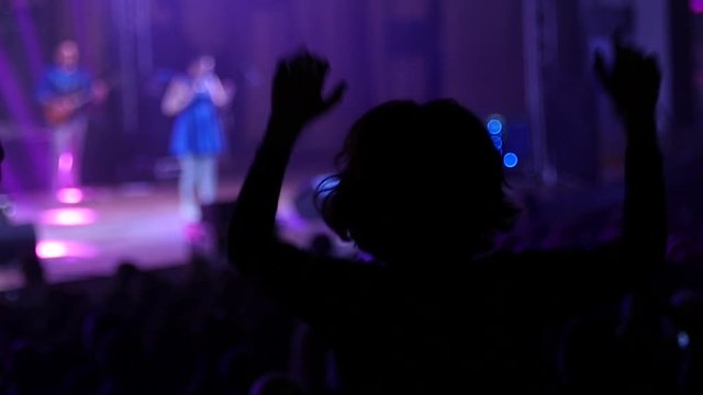 Dancing girl fan silhouettes on a concert flashing light cheerful hands in air