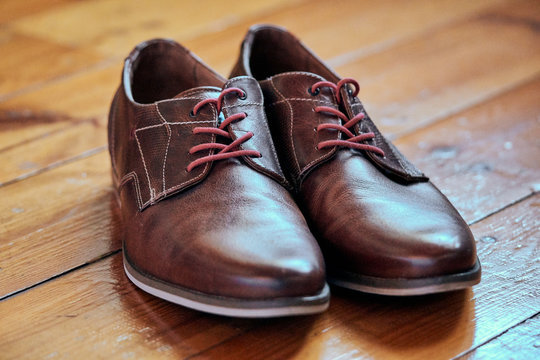 Brown leather shoes of a groom with red shoe laces on a wooden floor