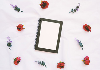 Flat lay style of blank card on notebook with flowers decorated on white cloth, top view