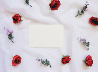 Flat lay style of blank card with flowers decorated on white cloth, top view