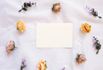 Flat lay style of blank card with flowers decorated on white cloth, top view