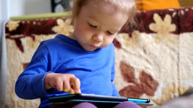 Little girl on a couch playing tablet computer game sliding touchscreen