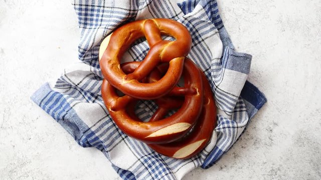 Three german fresh baked pretzel buns placed on white and blue checkered napkin. Stone background. Shot from above.
