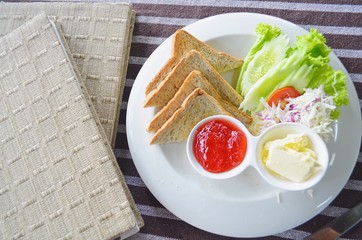  Toast with jam and butter in a white plate on a beautiful tablecloth.