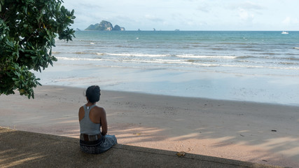 Fototapeta premium Woman sitting on sidewalk at beach looking at islands