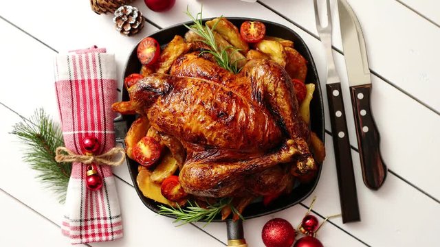 Top view of Baked whole chicken or turkey served in iron square pan with beautiful Christmas decoration around. Placed on white rustical wooden background.