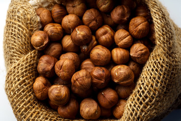 Close up with a handful of raw hazelnuts in textile bag on white background. Overhead image