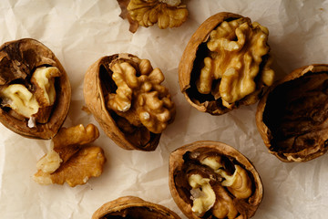 Raw walnuts in cracked nutshells on parchment paper. Overhead view
