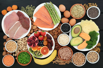 Super food for body builders high in protein including meat, fish, dairy, multi vitamin and fish oil tablets, legumes, fruit, cereals, vegetables, herbs, nuts and seeds on dark wood background.