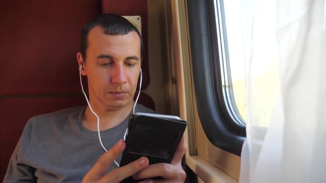man listening to the music on the train rail car coupe compartment travel. slow motion video. man with a smartphone at the window of a train in a lifestyle car travel internet social media web. man