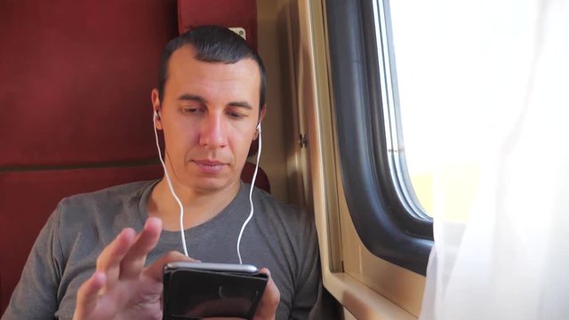 man listening to the music on the train journey rail car coupe compartment travel. slow motion video. man with a smartphone at the window of a train in a car travel internet social media web lifestyle