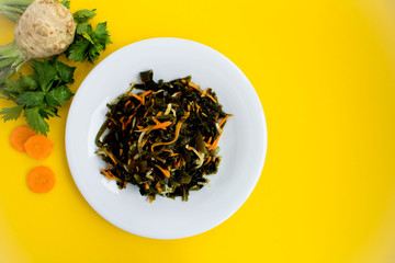 Salad with seaweed, celery and carrots in the  white plate on the yellow background.Top view.Copy space.