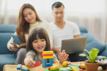 Family time Daughter laughing enjoying playing a game but her mother reading a book and her father working with laptop which sitting on sofa at home