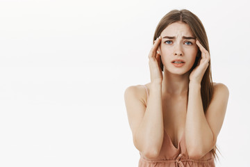 Woman having headache during periods feeling frustrated and concerned touching temples frowning from discomfort suffering from painful feeling or migraine standing concerned over gray background
