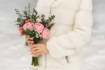 Winter wedding. Bride in mink coat holding bouquet of flowers in winter