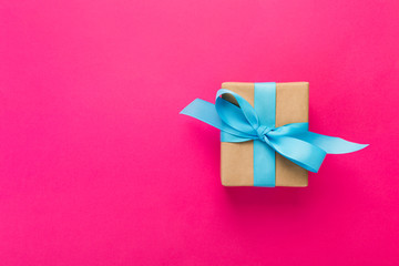 gift wrapped and decorated with blue bow on pink background with copy space. Flat lay, top view