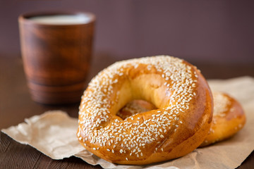 Two bagel with sesame and cup of milk on a dark wooden table. Side view, close up