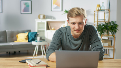 Portrait Shot of a Handsome Smiling Man Working on a Laptop at Her Desk in the Cozy Living Room.