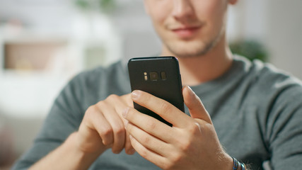 Close-up shot of the Handsome Young Man Using Smartphone, Browsing in Internet, Checking Social Networks while Sitting At Home.