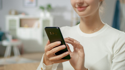 Portrait of the Beautiful Young Woman Using Smartphone, Browsing in Internet, Checking Social Networks while Sitting At Home.