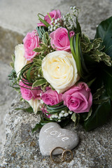 Un bouquet de mariée à cotés de 2 alliances et une pierre où est écrit 