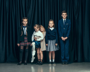 Cute surprised stylish children on dark background. Beautiful stylish teen girls and boy standing together and posing on the school stage in front of the curtain. Classic style. Kids fashion and