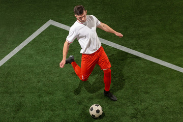 Football player tackling for ball over green grass background. Professional football soccer player in motion at studio. Fit jumping man in action, jump, movement at game.