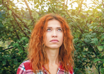 Beautiful red-haired woman, portrait on the background of the branches in the garden, the rays of the evening sun
