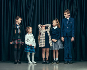 Cute surprised stylish children on dark background. Beautiful stylish teen girls and boy standing together and posing on the school stage in front of the curtain. Classic style. Kids fashion and