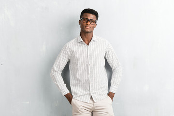 Young afro american man with glasses posing on textured grey wall