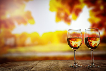 Two glasses with wine on a wooden table in an autumn setting   