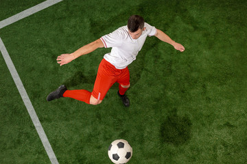 Football player tackling for ball over green grass background. Professional football soccer player in motion at studio. Fit jumping man in action, jump, movement at game.